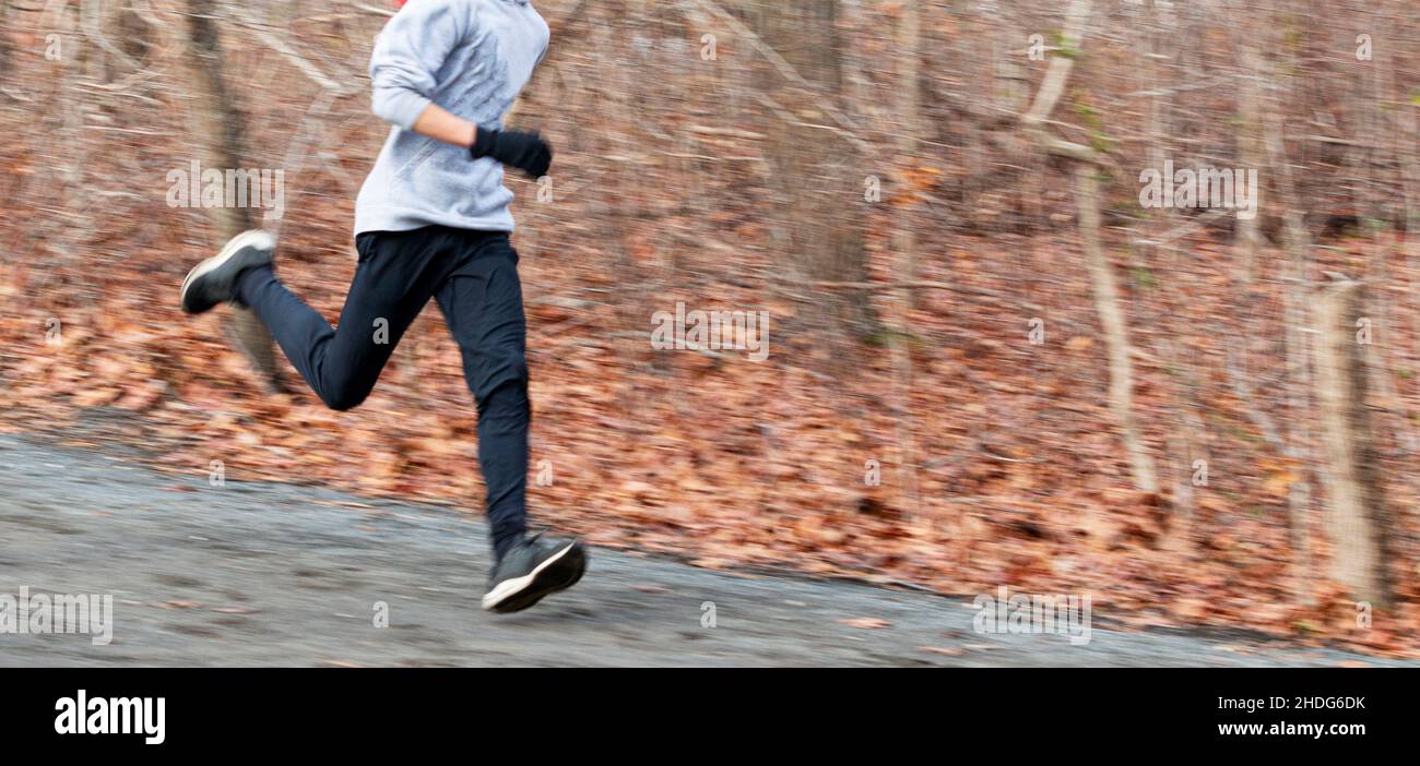 Coureur flou montrant la vitesse de descente sur un chemin de terre dans les bois pendant la pratique de piste d'école secondaire. Banque D'Images