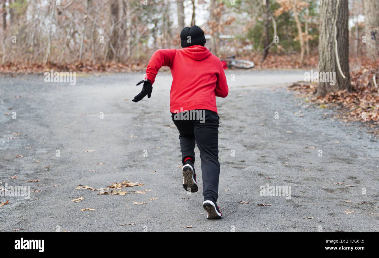 Vue arrière d'un garçon de l'école secondaire qui s'incline rapidement dans les bois lors d'un entraînement de vitesse sur piste et sur le terrain lors d'un hiver froid Banque D'Images