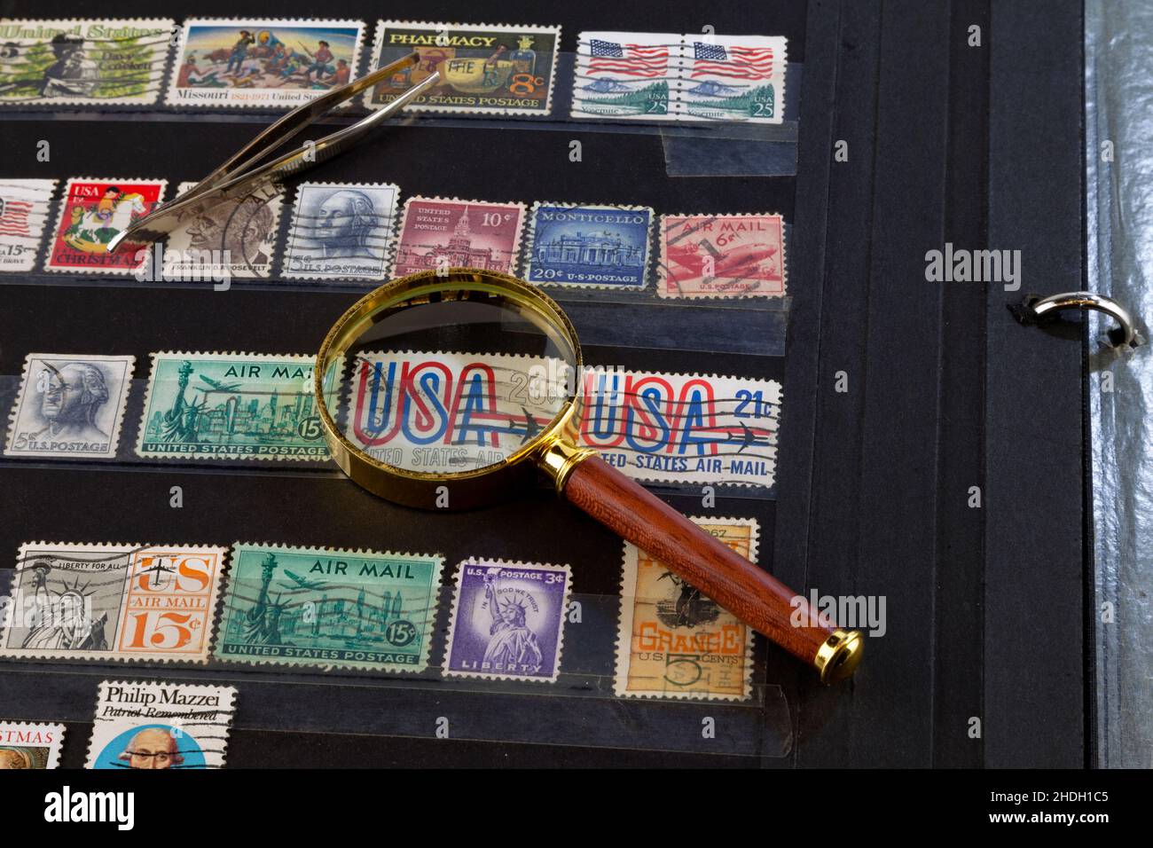 Une pince à timbres et une loupe sur le dessus d'un classeur à timbres rempli d'anciens timbres américains. Banque D'Images