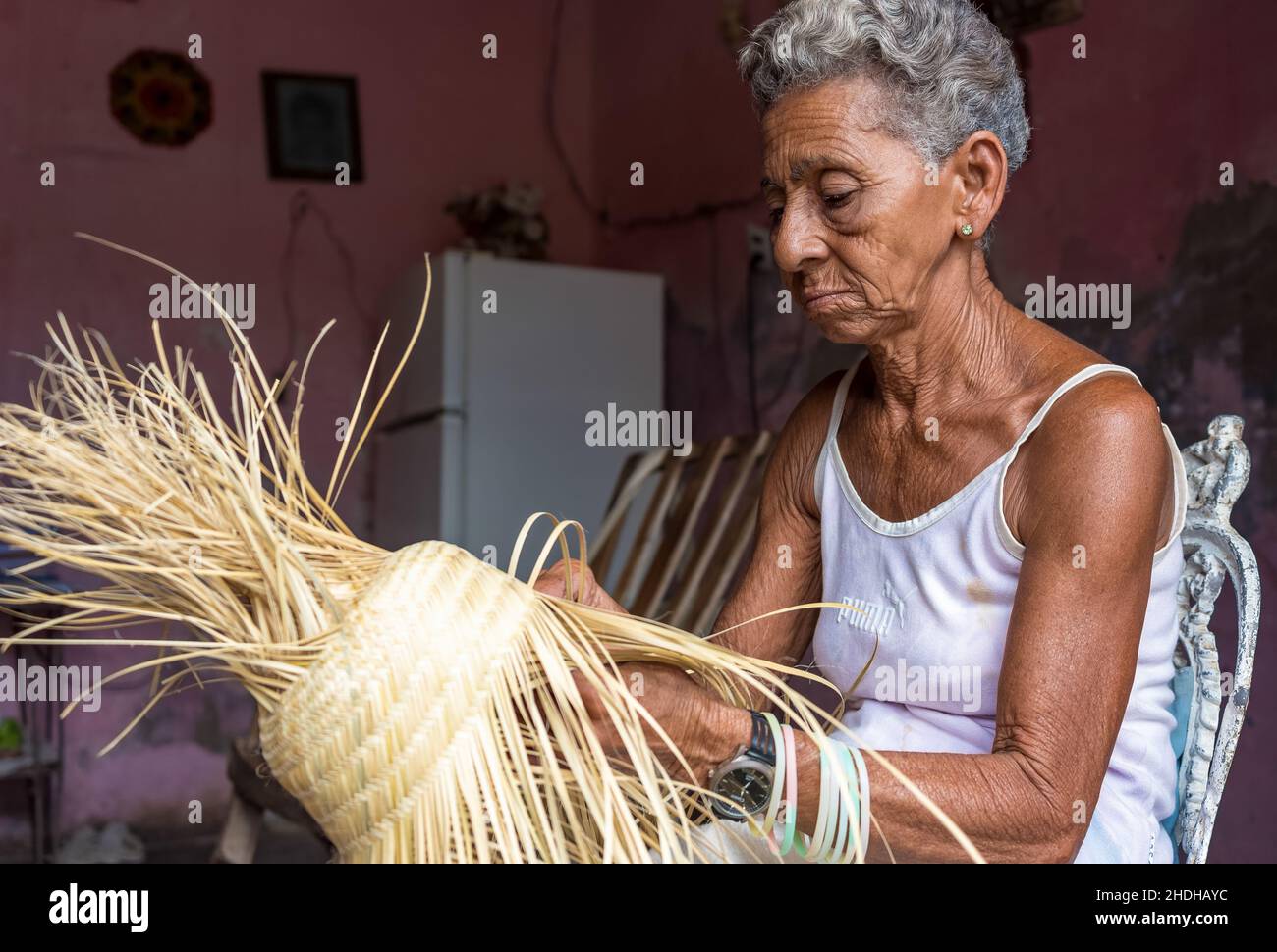 Portrait d'une femme afro-caribéenne senior qui fait un chapeau de paille qui est un souvenir traditionnel.Elle travaille dans le salon de sa maison.6 janvier Banque D'Images