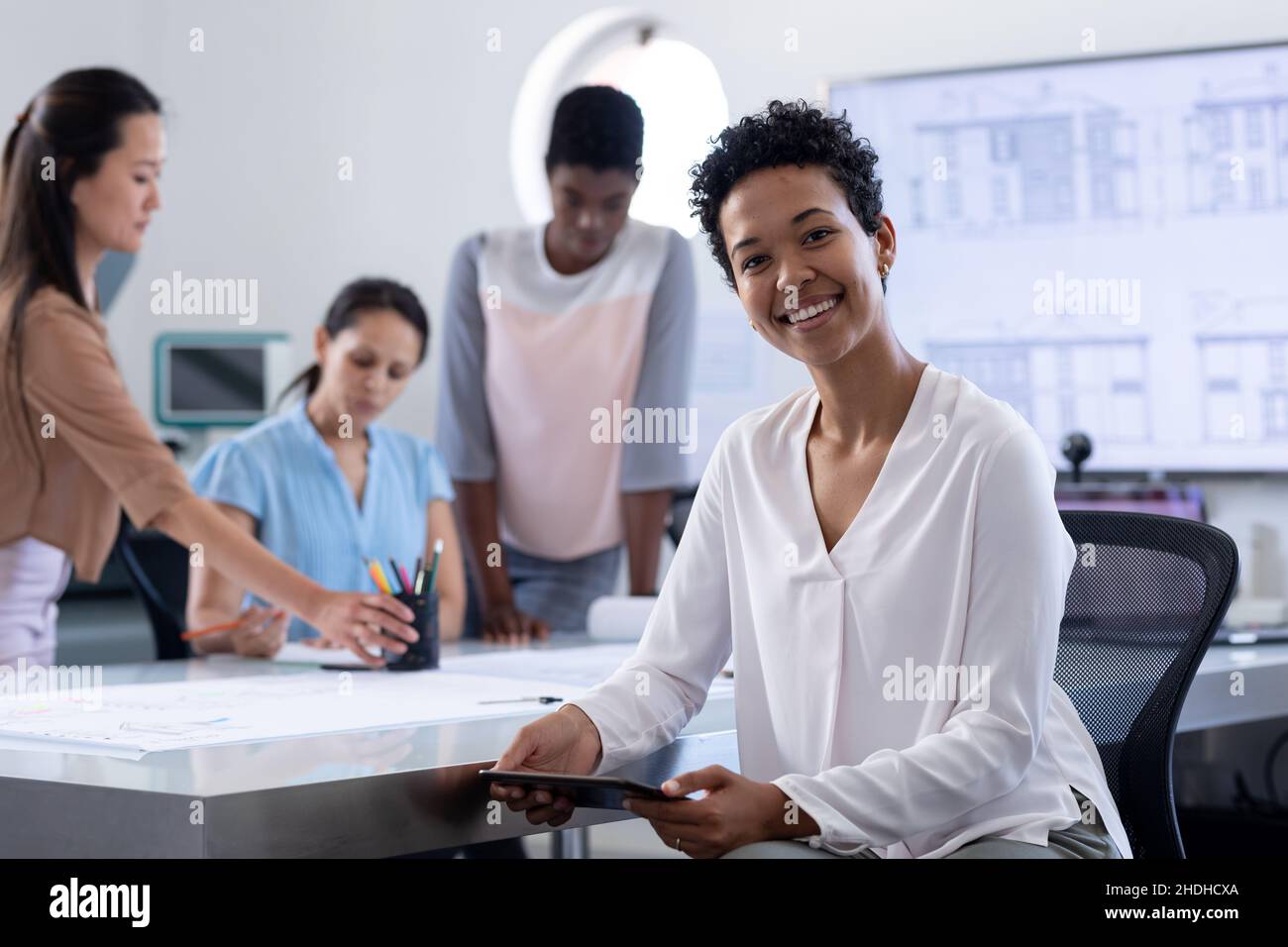 Portrait d'une femme d'affaires souriante assise à la table de conférence pendant que ses collègues sont en arrière-plan Banque D'Images