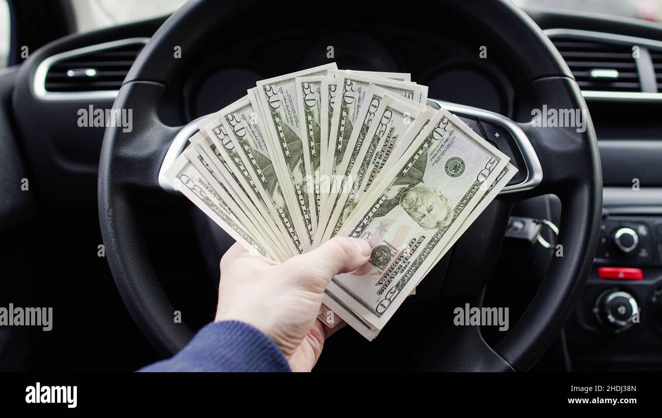 Un dollar facture dans la main mâle sur le fond du volant dans la voiture.Notion de revenus ou de pots-de-vin, assurance ou crédit, investissement ou s. Banque D'Images