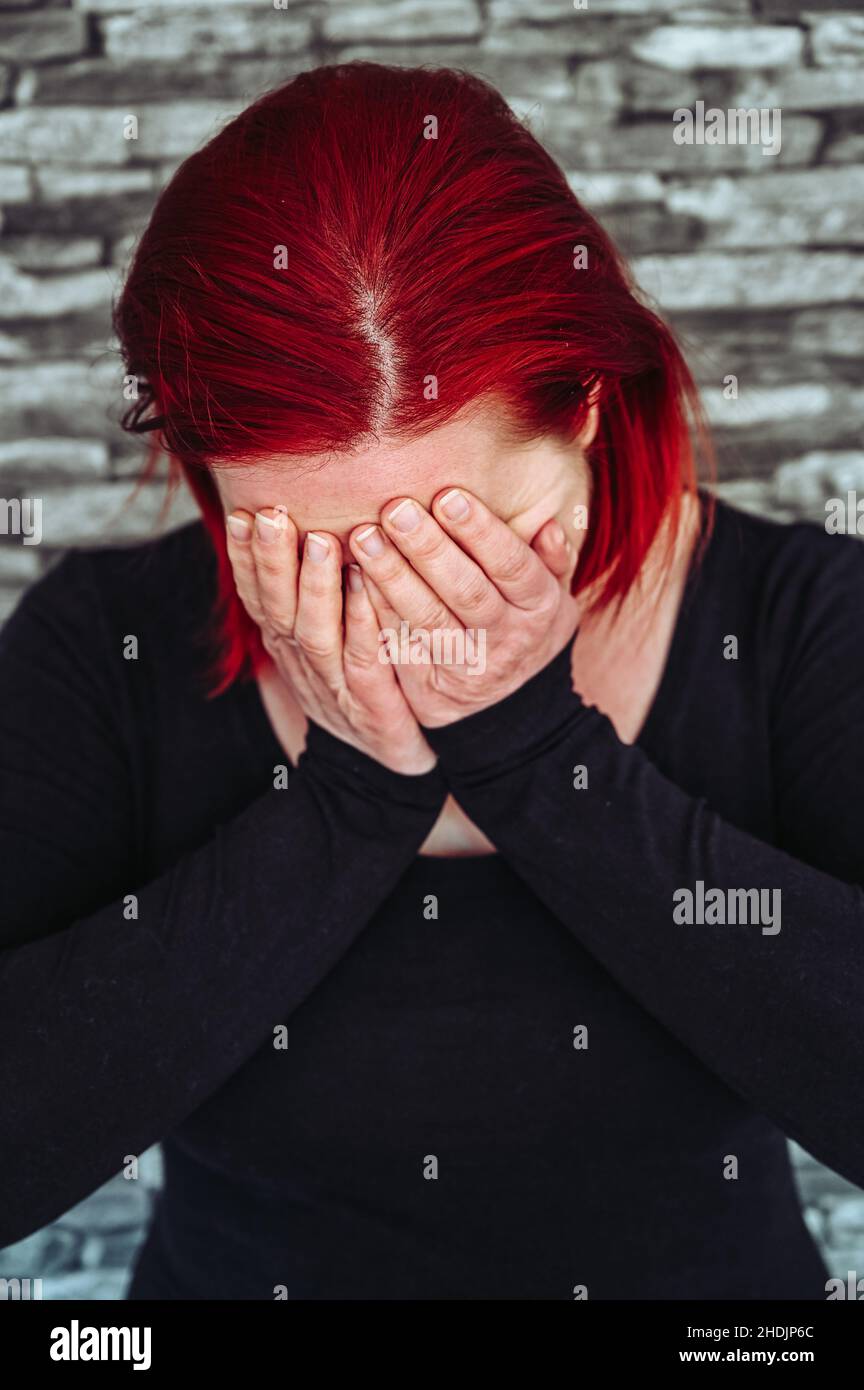 Une femme désespérée aux cheveux rouges de 30-35 ans tient ses mains devant son visage Banque D'Images