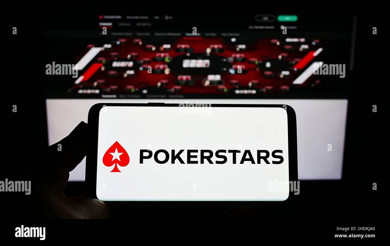 Personne tenant un smartphone avec le logo de la salle de poker en ligne PokerStars sur l'écran devant le site Web.Mise au point sur l'affichage du téléphone. Banque D'Images