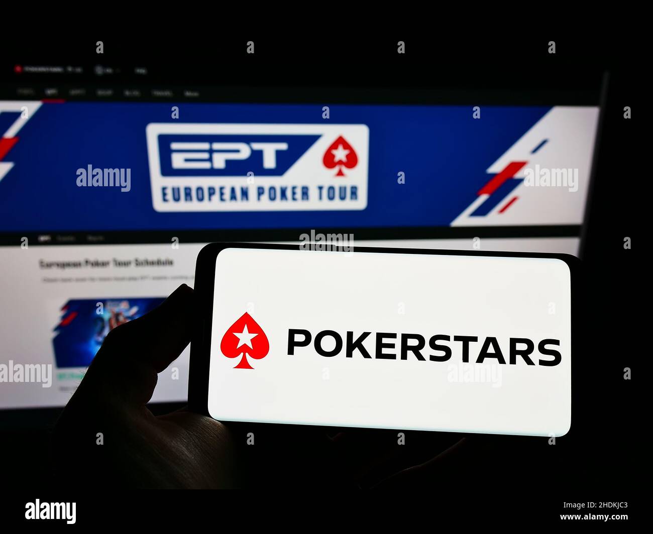 Personne tenant le téléphone mobile avec le logo de la salle de poker en ligne PokerStars sur l'écran en face de la page Web d'affaires.Mise au point sur l'affichage du téléphone. Banque D'Images