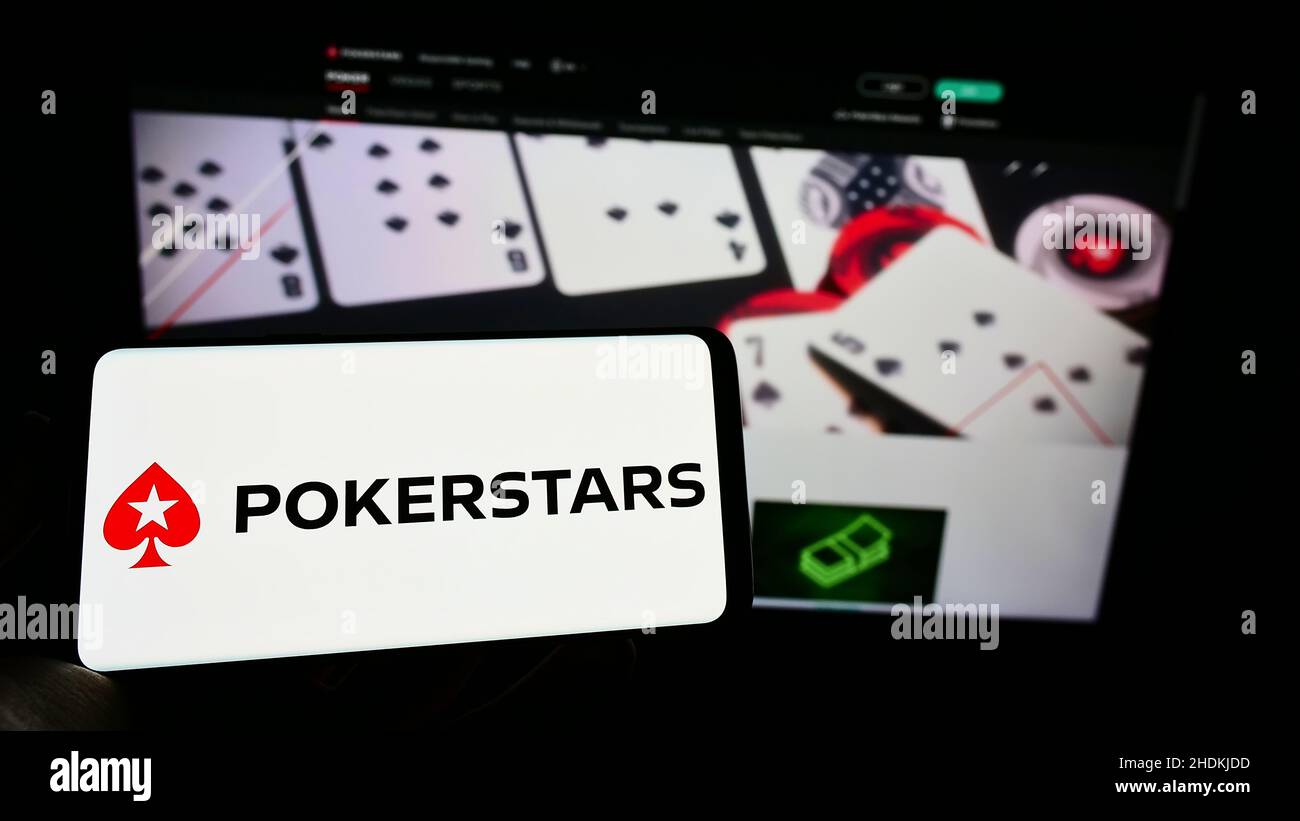 Personne tenant le téléphone portable avec le logo de la salle de poker en ligne PokerStars sur l'écran en face de la page web de l'entreprise.Mise au point sur l'affichage du téléphone. Banque D'Images