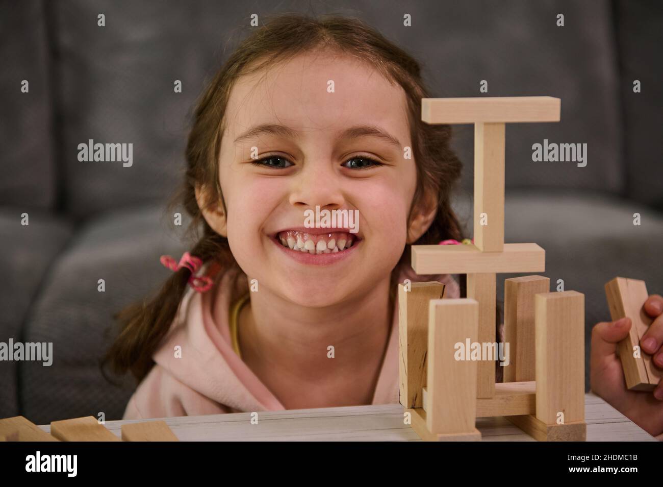 Portrait en gros plan d'une belle adorable petite fille souriant, souriant, regardant l'appareil photo, appréciant le jeu de société éducatif, construisant une structure en bois Banque D'Images