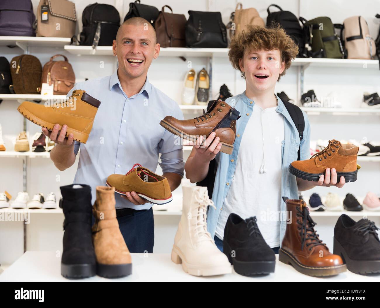 Un homme heureux et un garçon adolescent dans un magasin de chaussures avec  des mocassins et des bottes entre les mains Photo Stock - Alamy