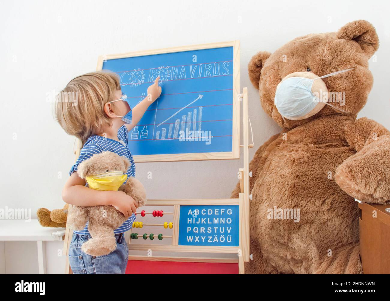 Mignon enfant garçon dans la quarantaine à la maison jouer avec des jouets portant des masques médicaux et le graphique de croissance des cas de COVID-2019 tirés sur un tableau noir, pendant coro Banque D'Images