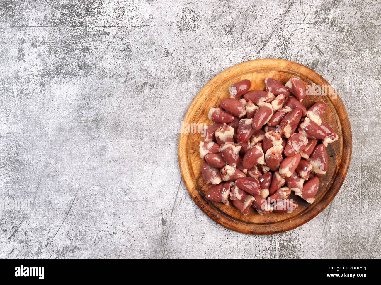 Cœurs de poulet crus sur une planche à découper ronde en bois sur fond gris foncé. Vue de dessus, plan d'appartement Banque D'Images