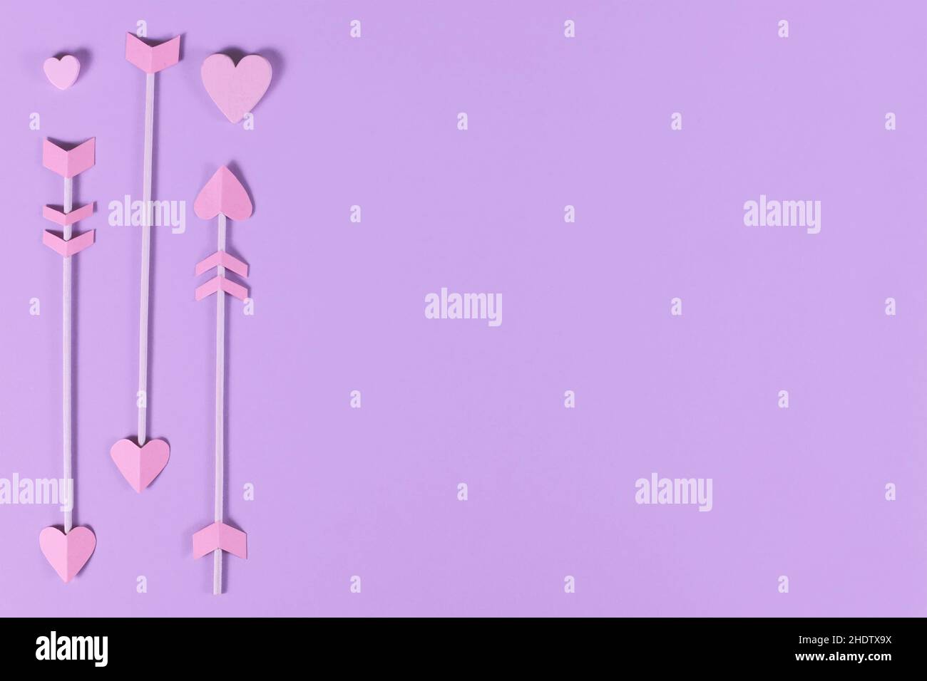 Flèches de cupidon rose avec pointes en forme de coeur sur fond violet avec espace de copie Banque D'Images