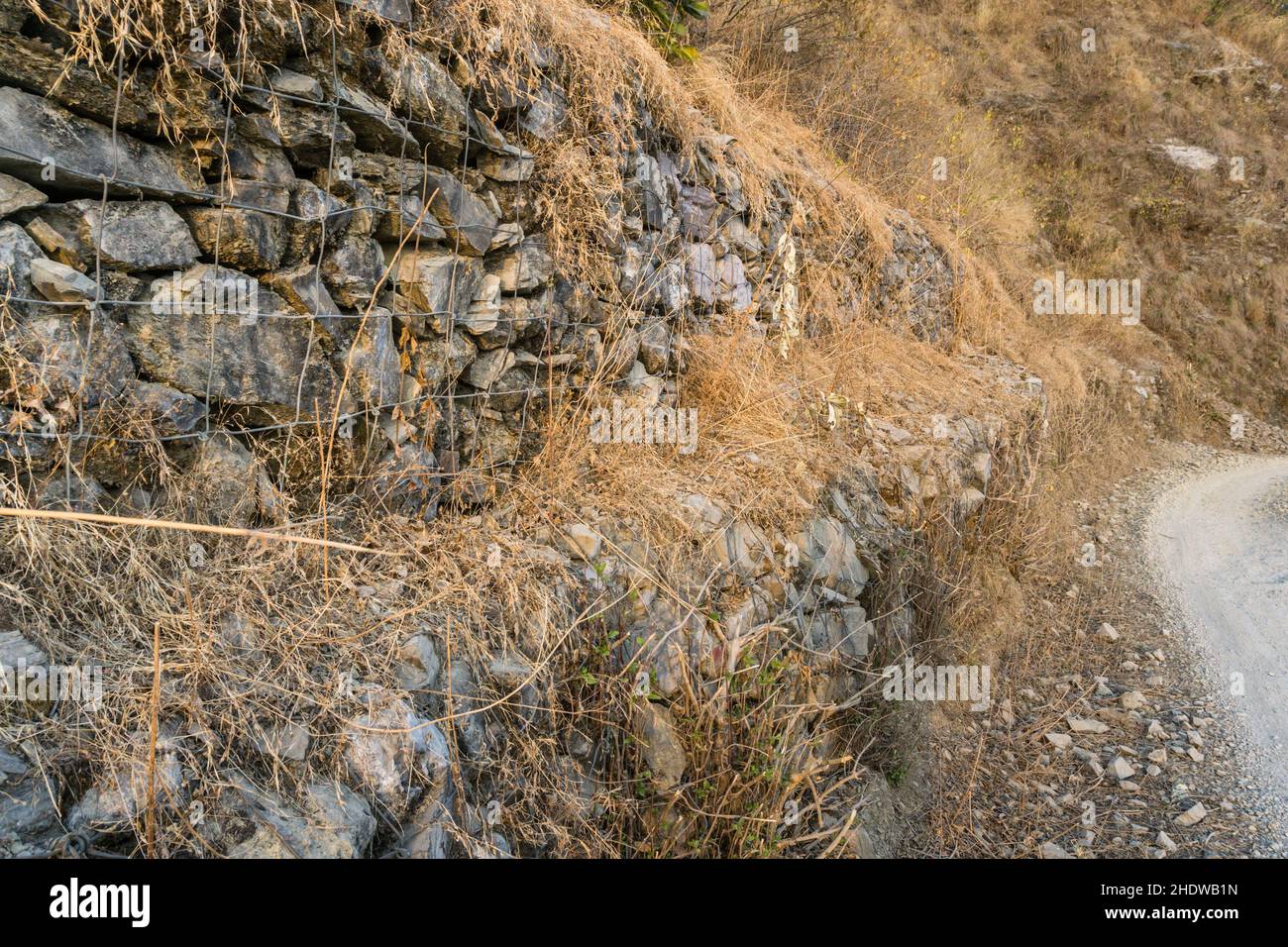 Un mur de pierre de bord de route recouvert de mousse et d'herbe sèche. Ces types de murs de pierre sont généralement construits dans les régions de montagne pour éviter les glissements de terrain et la route c Banque D'Images