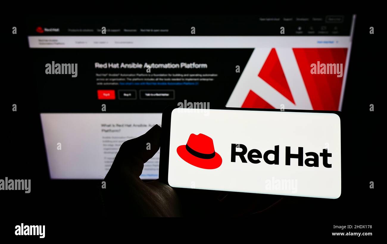 Personne tenant un téléphone portable avec le logo de la société américaine de logiciels Red Hat Inc. À l'écran en face de la page Web d'affaires.Mise au point sur l'affichage du téléphone. Banque D'Images