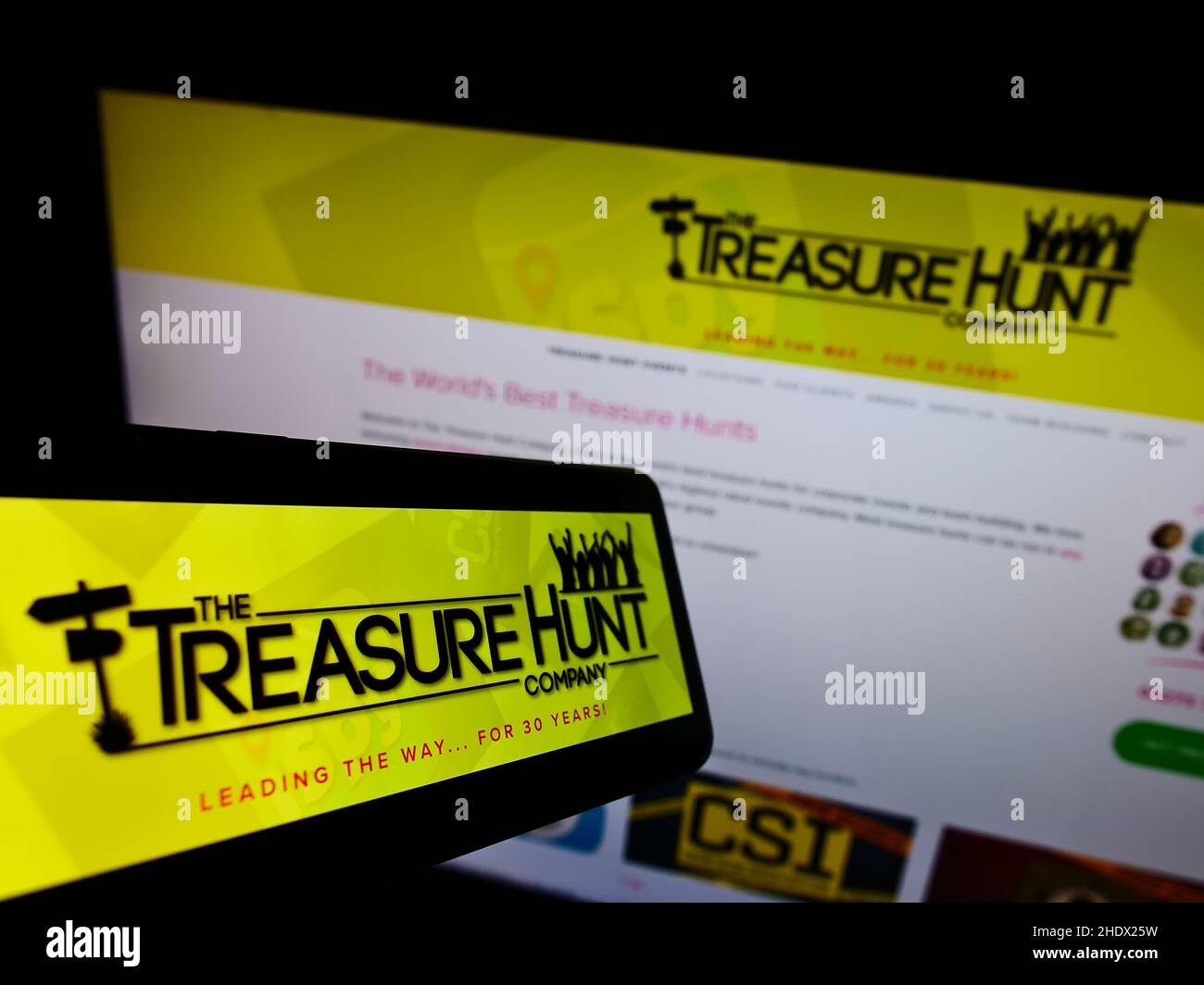 Smartphone avec logo de Treasure Hunt Company (Brighton) sur écran en face du site Web d'entreprise.Effectuez la mise au point au centre-droit de l'écran du téléphone. Banque D'Images