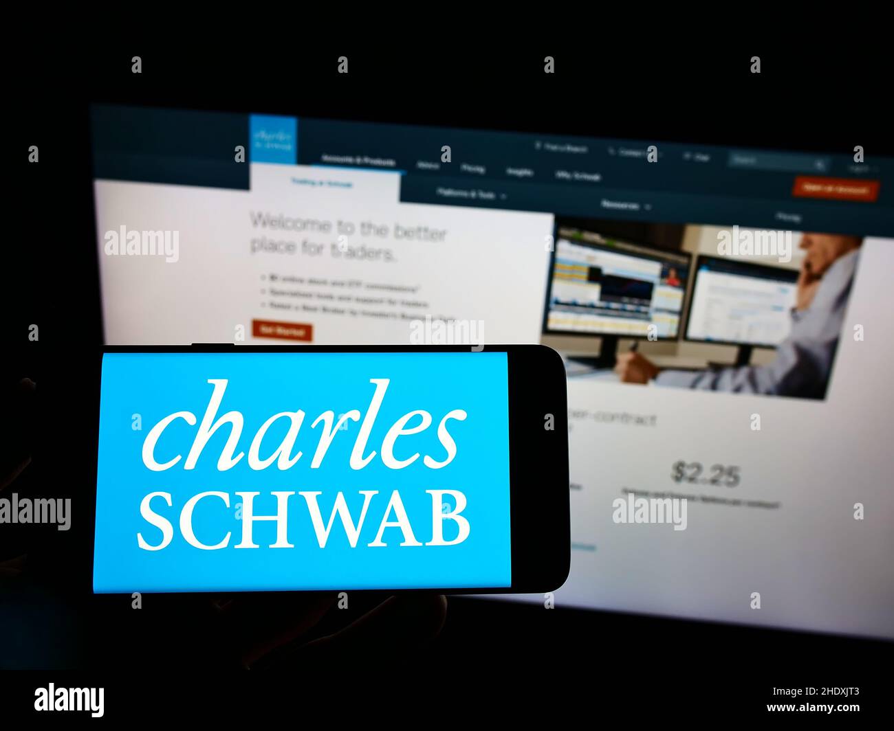Personne tenant un téléphone portable avec le logo de la société financière américaine The Charles Schwab Corporation à l'écran en face de la page web.Mise au point sur l'affichage du téléphone. Banque D'Images