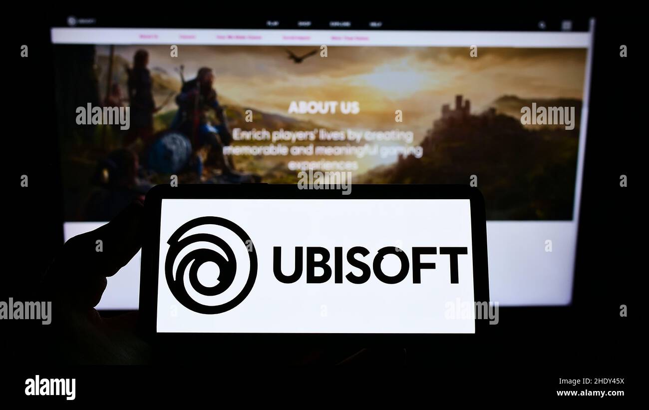 Personne tenant un smartphone avec le logo de la société française de jeux vidéo Ubisoft Entertainment sa à l'écran devant le site Web.Mise au point sur l'affichage du téléphone. Banque D'Images