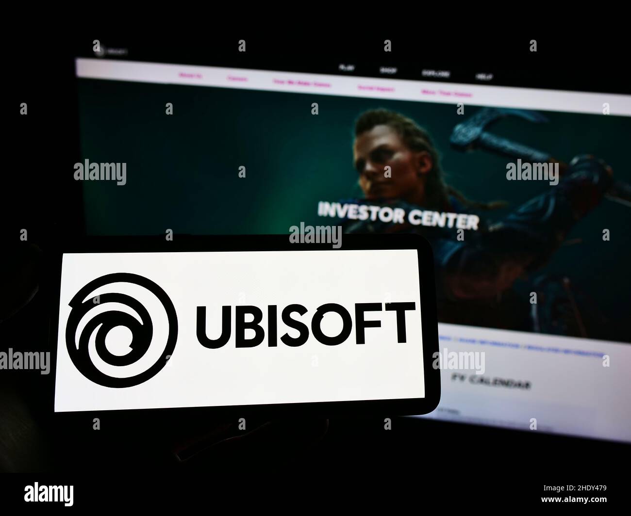 Personne tenant un téléphone portable avec le logo de la société française de jeux vidéo Ubisoft Entertainment sa à l'écran en face de la page Web.Mise au point sur l'affichage du téléphone. Banque D'Images