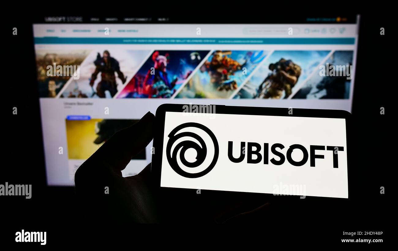 Personne tenant un téléphone portable avec le logo de la société française de jeux vidéo Ubisoft Entertainment sa à l'écran en face de la page web.Mise au point sur l'affichage du téléphone. Banque D'Images