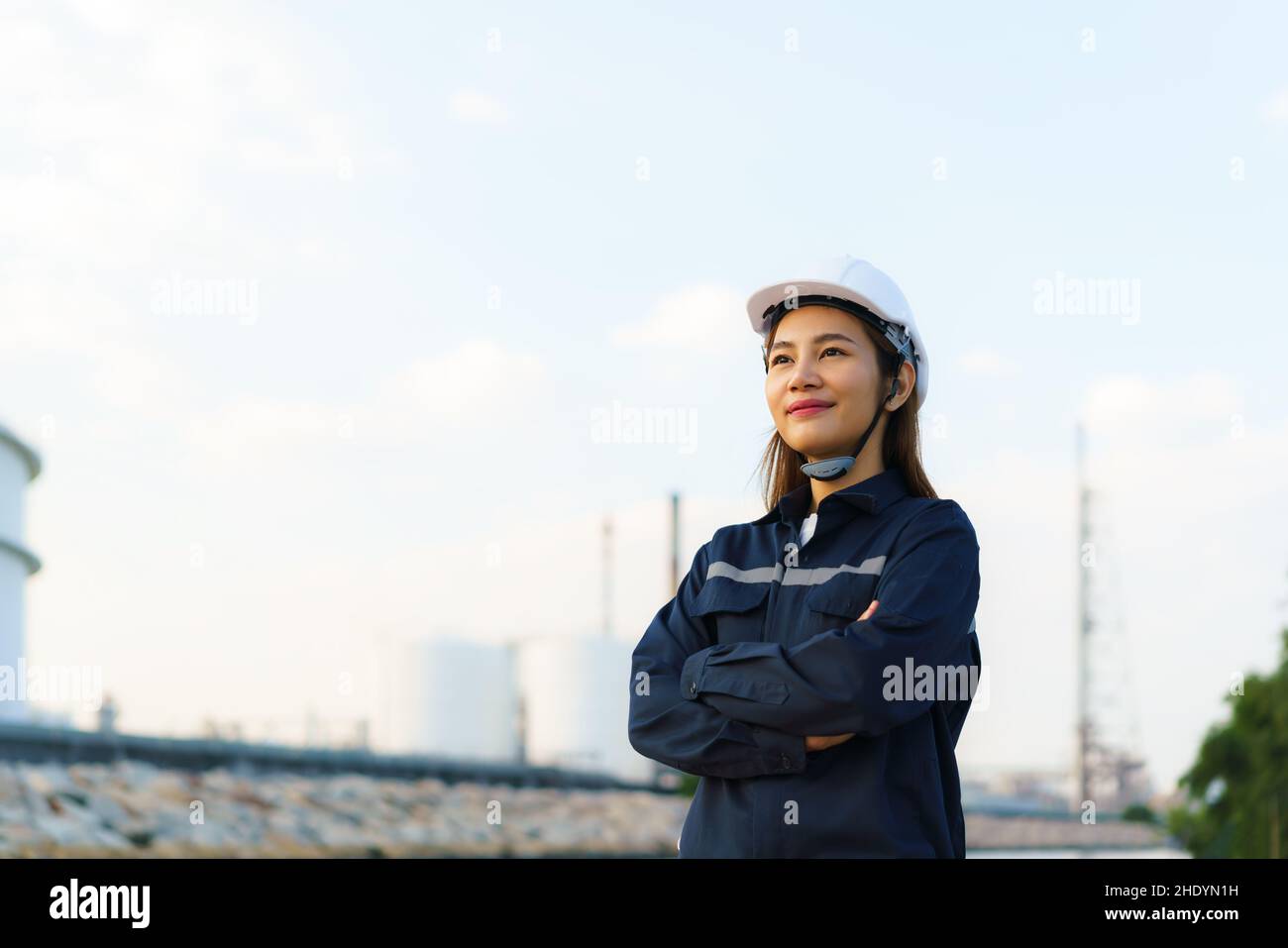 Une femme asiatique a croisé un bras et sourire avec confiance en vue de l'avenir avec l'usine de raffinerie de pétrole en arrière-plan. Banque D'Images