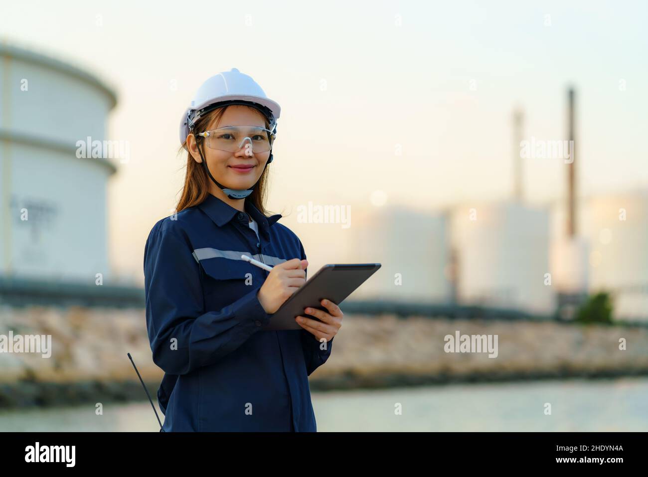 Une femme d'ingénieur asiatique vérifie la maintenance de l'usine de raffinerie de pétrole le soir via des tablettes numériques. Banque D'Images