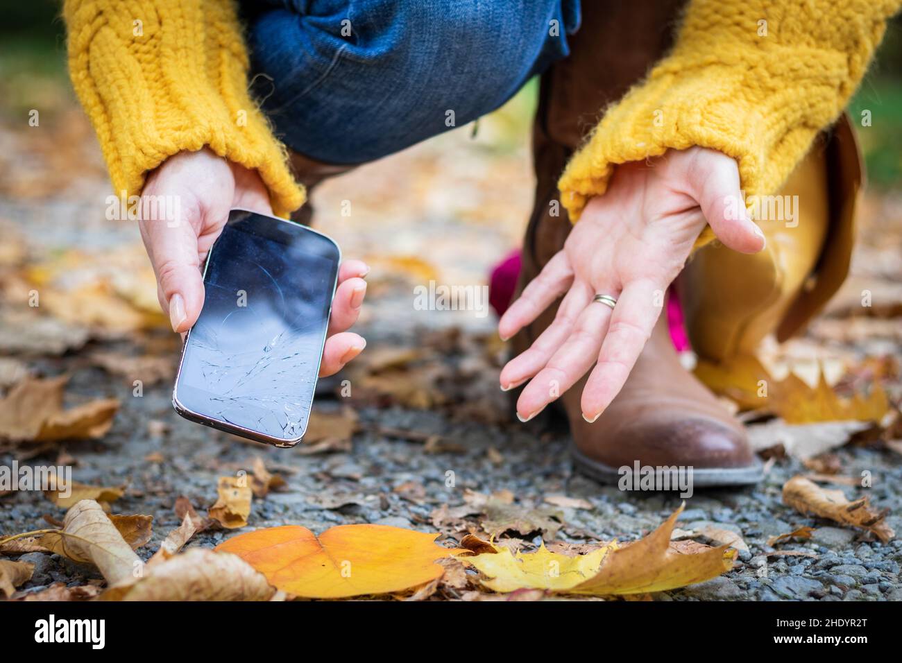Femme contrariée et smartphone cassé.Une femme prend un téléphone portable endommagé par terre. Banque D'Images