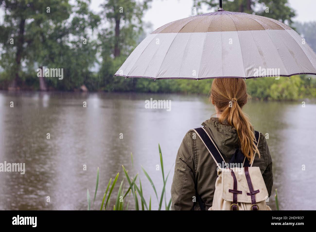 Femme inquiète avec un parapluie regardant le niveau de la rivière en hausse pendant une inondation.Saison des pluies, catastrophe naturelle. Banque D'Images