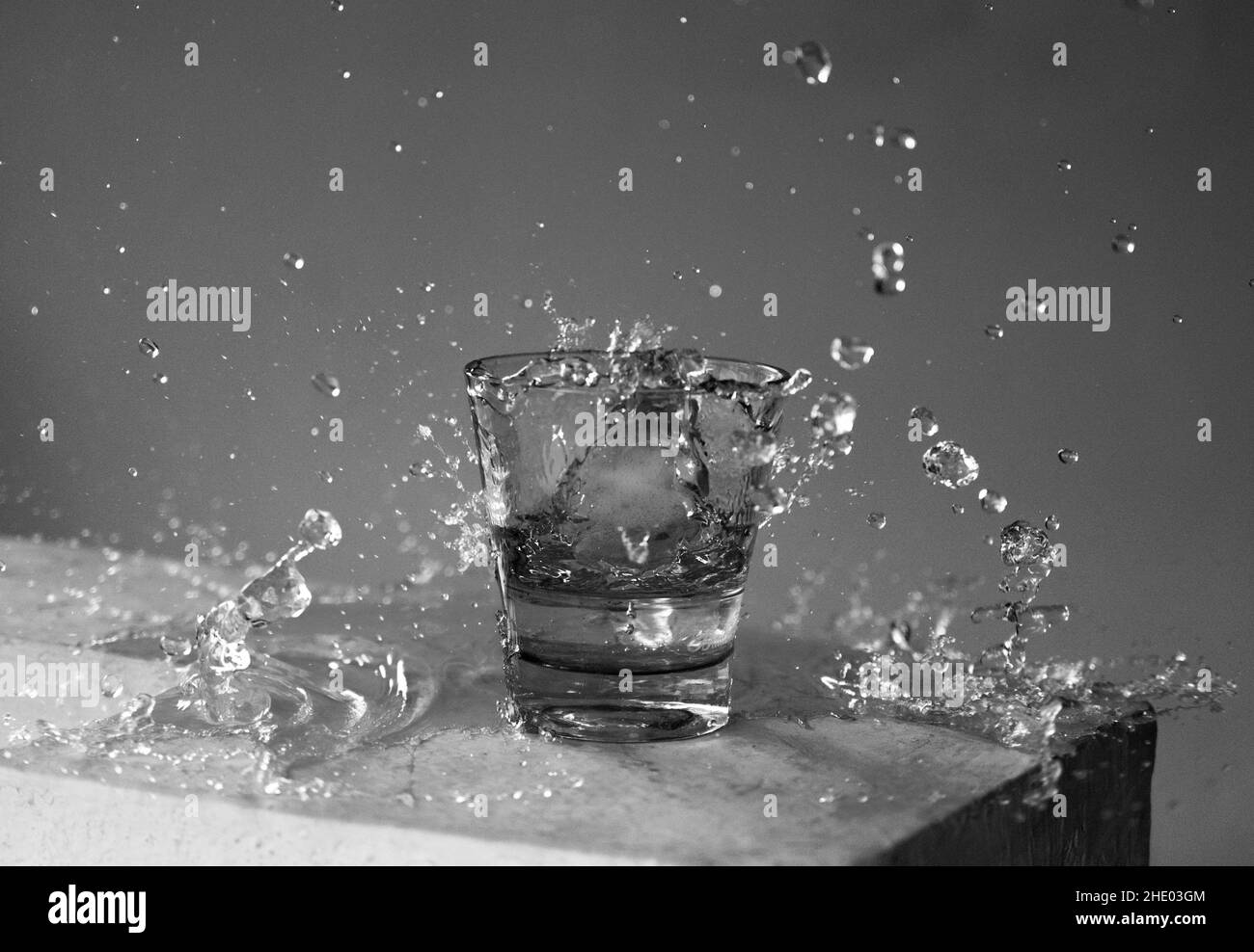 Belle photo d'un verre d'eau et éclaboussures autour de lui en niveaux de gris Banque D'Images