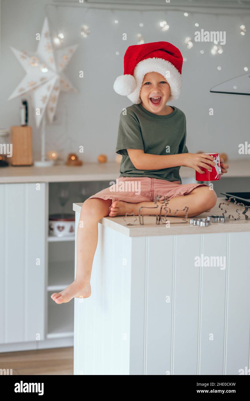 Un petit garçon dans un chapeau de père Noël et de boire du lait de cacao assis sur la table de cuisine Banque D'Images