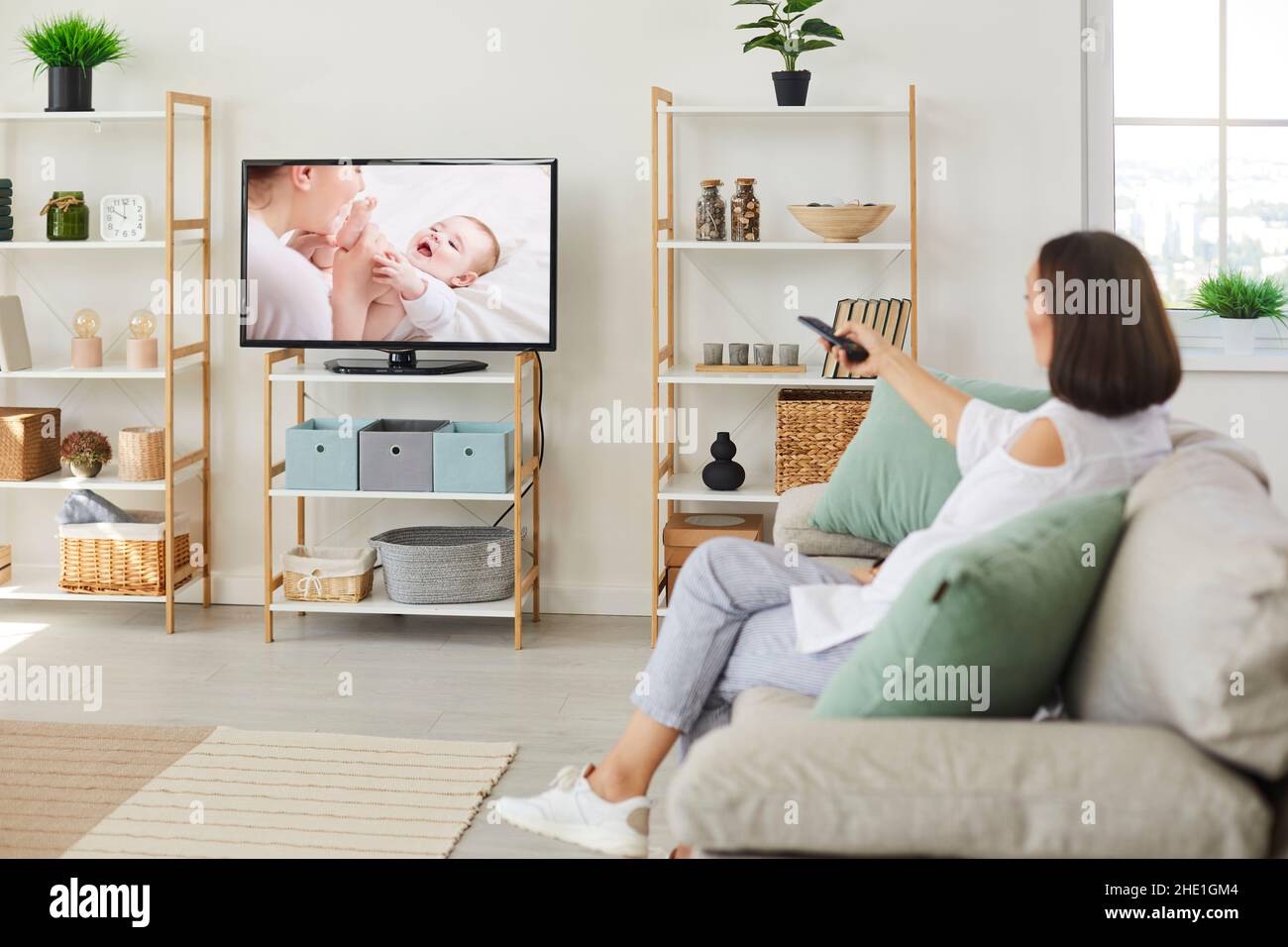 Femme assise sur un canapé à la maison et regardant un film à la télévision avec grand écran Banque D'Images