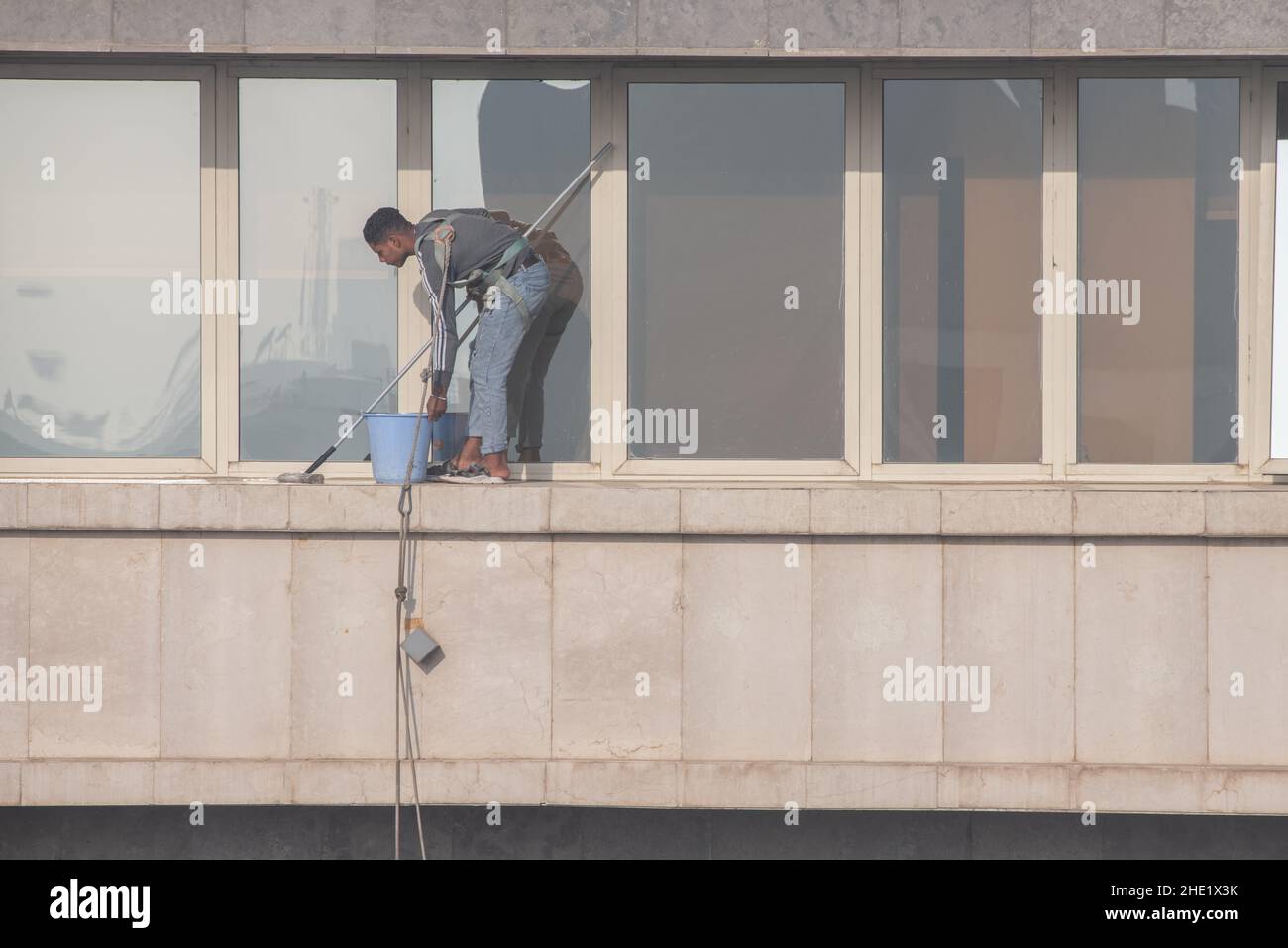 Un lave-glace au Caire, en Égypte travaille à nettoyer le verre d'un bâtiment de plusieurs étages.Travail dangereux avec un minimum d'équipement de sécurité. Banque D'Images