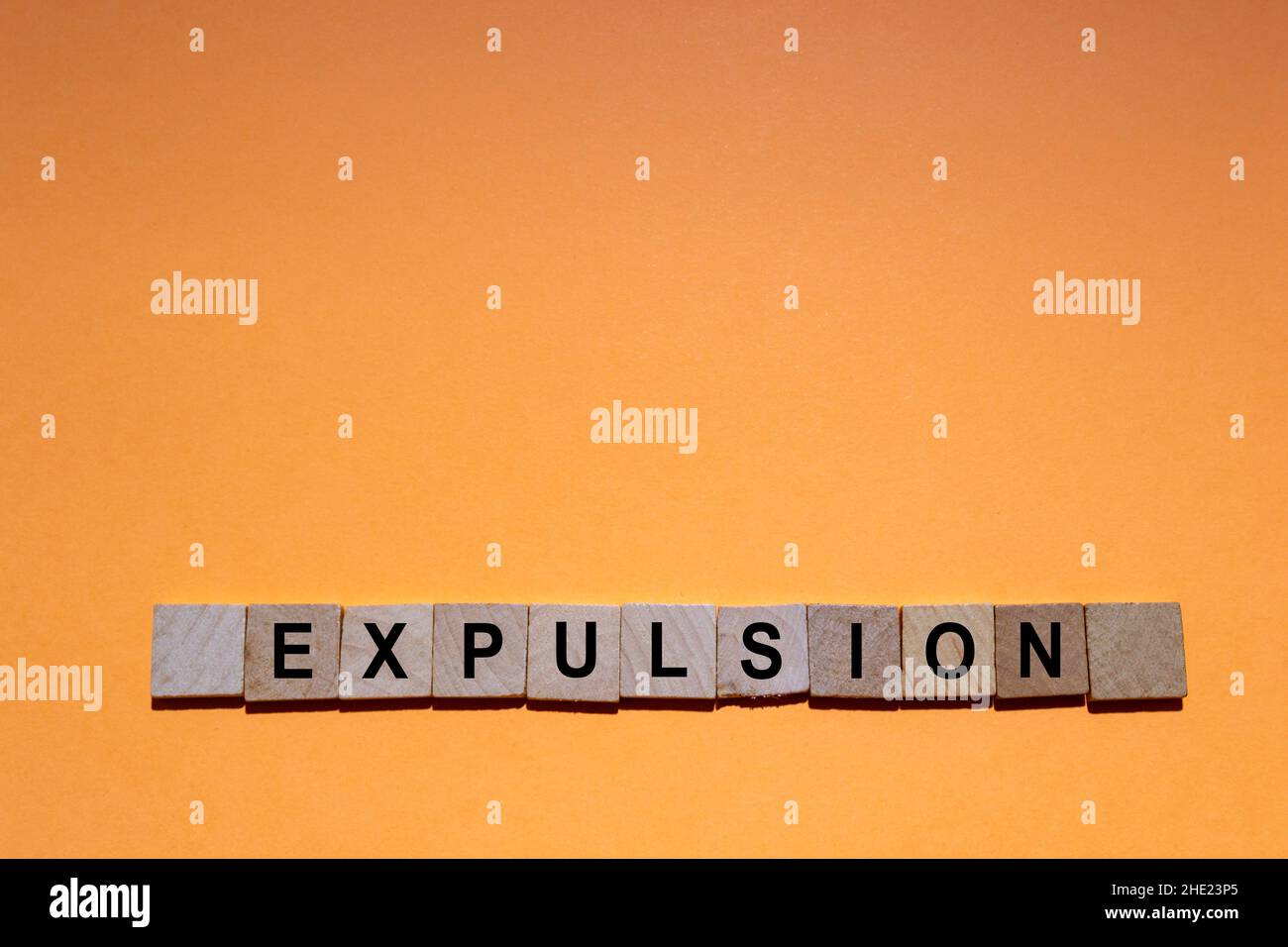 EXPULSION.Mot écrit sur des carreaux carrés en bois avec un fond orange.Photographie horizontale. Banque D'Images