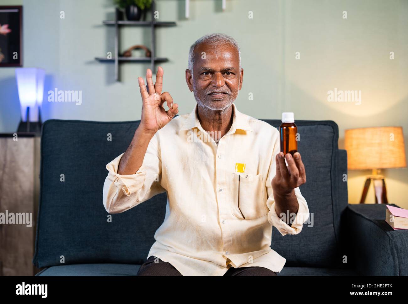 un vieil homme expérimenté et confiant qui explanification et recommante l'huile de vie de douleur en regardant la caméra à la maison - concept de l'influenceur, partage Banque D'Images