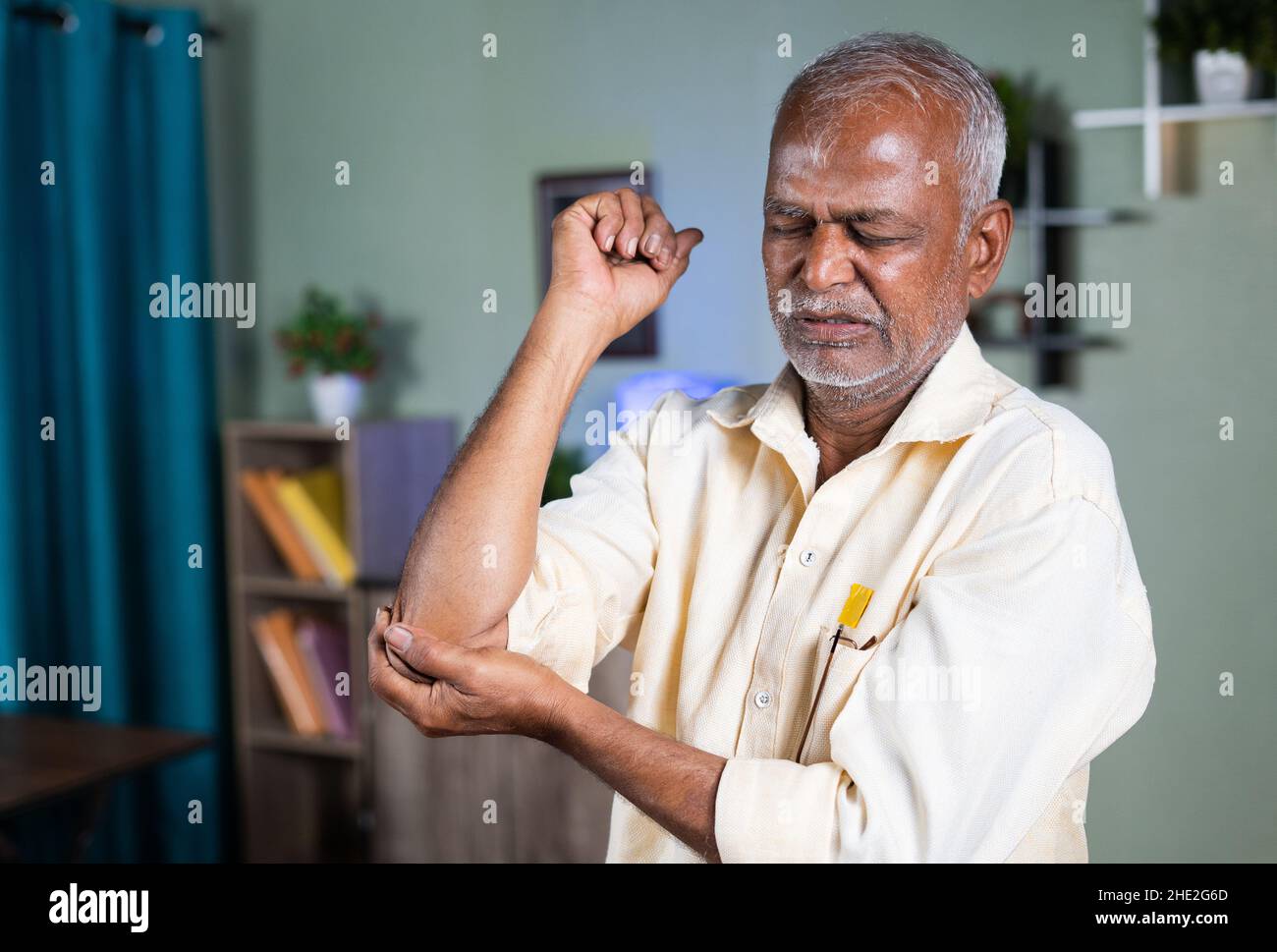 homme âgé indien s'exerçant par la main tentante en raison de douleurs articulaires au coude à la maison - concept de douleur articulaire et de blessure par entorse. Banque D'Images