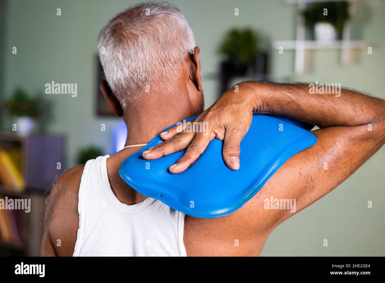 Vue arrière de l'homme ancien utilisant le sac d'eau chaude pour le soulagement de la douleur de cou - concept de thérapie naturelle d'eau chaude et de relaxation musculaire de la maison Banque D'Images