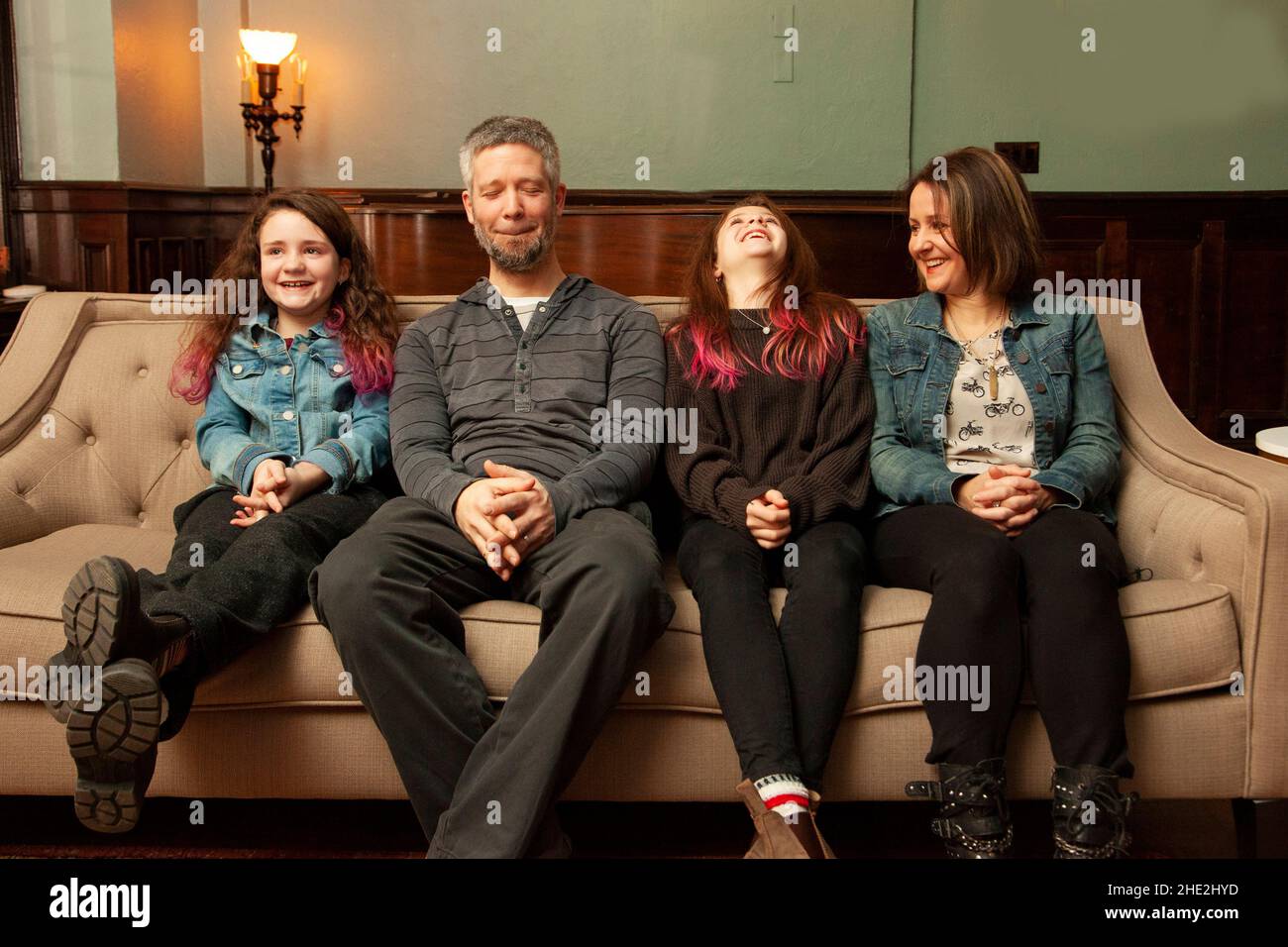une famille heureuse assise sur son canapé ayant un bon rire dur à quelque chose Banque D'Images