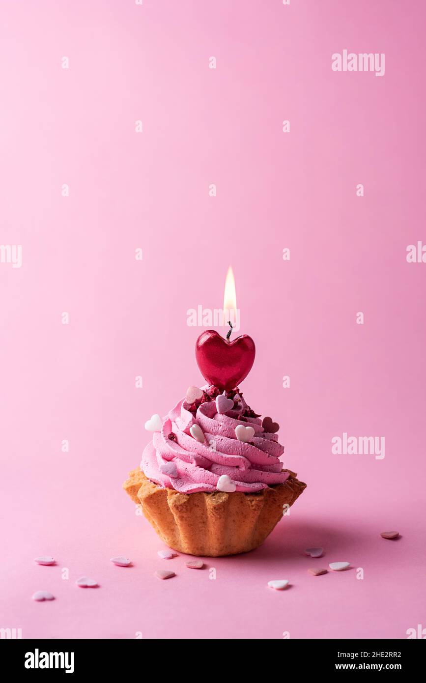 Carte de Saint-Valentin, cupcake à la crème et bougie rouge en forme de coeur sur fond rose. Banque D'Images