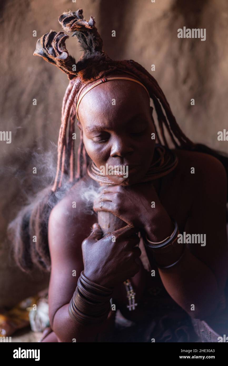 Femme Himba prenant quotidiennement bain de fumée dans sa hutte dans un village traditionnel Himba près de Kamanjab, Namibie du nord, Afrique. Banque D'Images