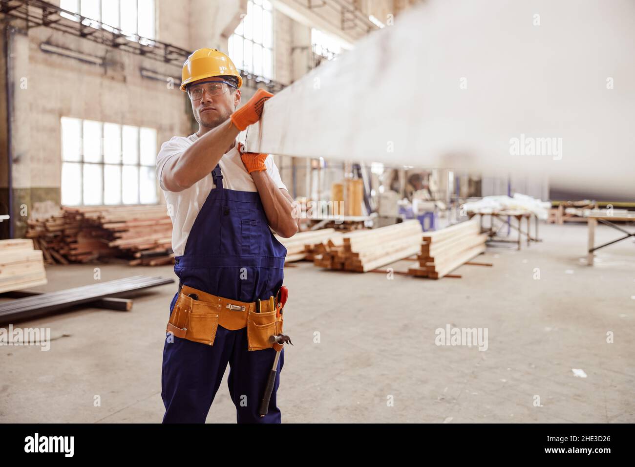 Homme sérieux constructeur transportant une planche en bois sur le chantier de construction Banque D'Images