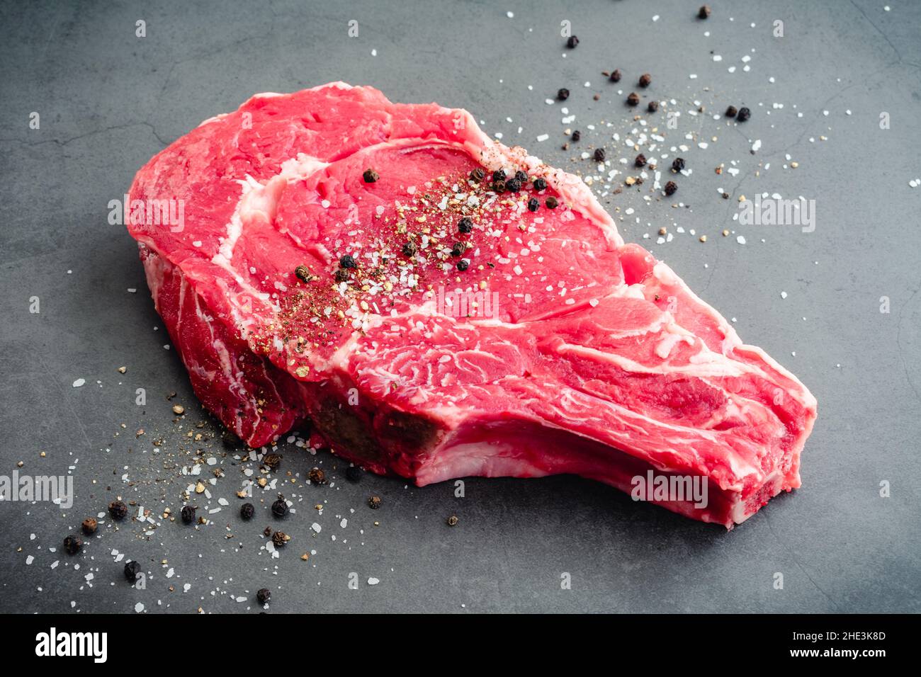 Steak de Ribeye à os brut assaisonné de sel casher et de poivre noir : steak de bœuf non cuit à os saupoudré de sel et de poivre Banque D'Images