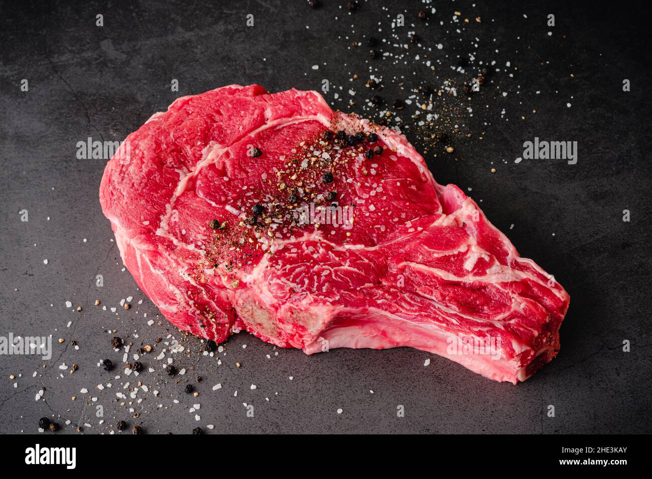 Steak de Ribeye à os brut assaisonné de sel casher et de poivre noir : steak de bœuf non cuit à os saupoudré de sel et de poivre Banque D'Images