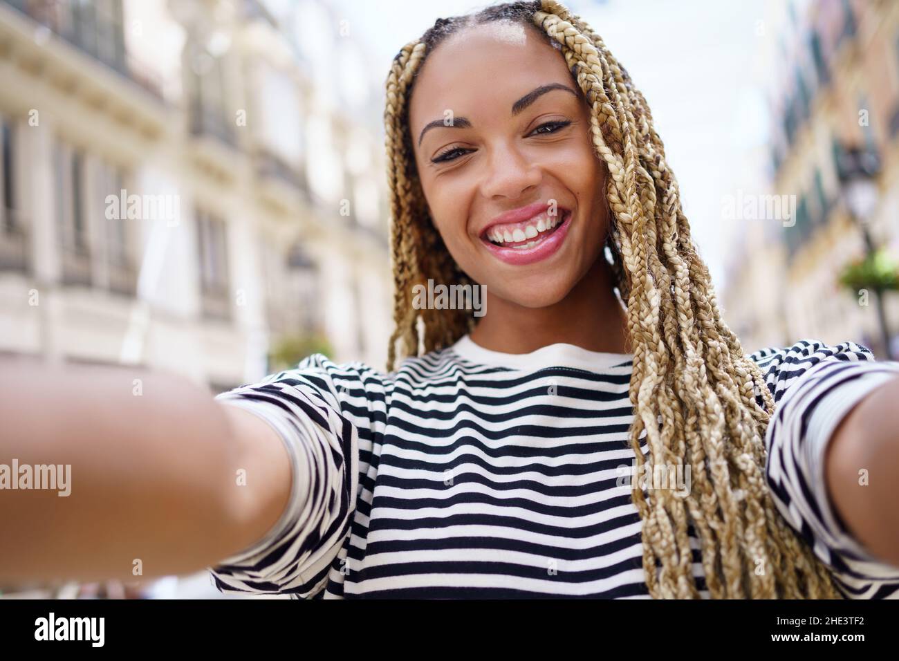 Fille noire avec des tresses afro prenant un selfie dans une rue urbaine avec un smartphone. Banque D'Images