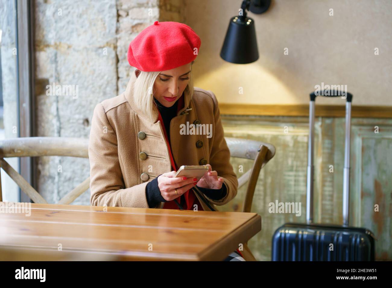 Femme voyageant pour le travail, attendant un café dans un café, tout en vérifiant son smartphone. Banque D'Images