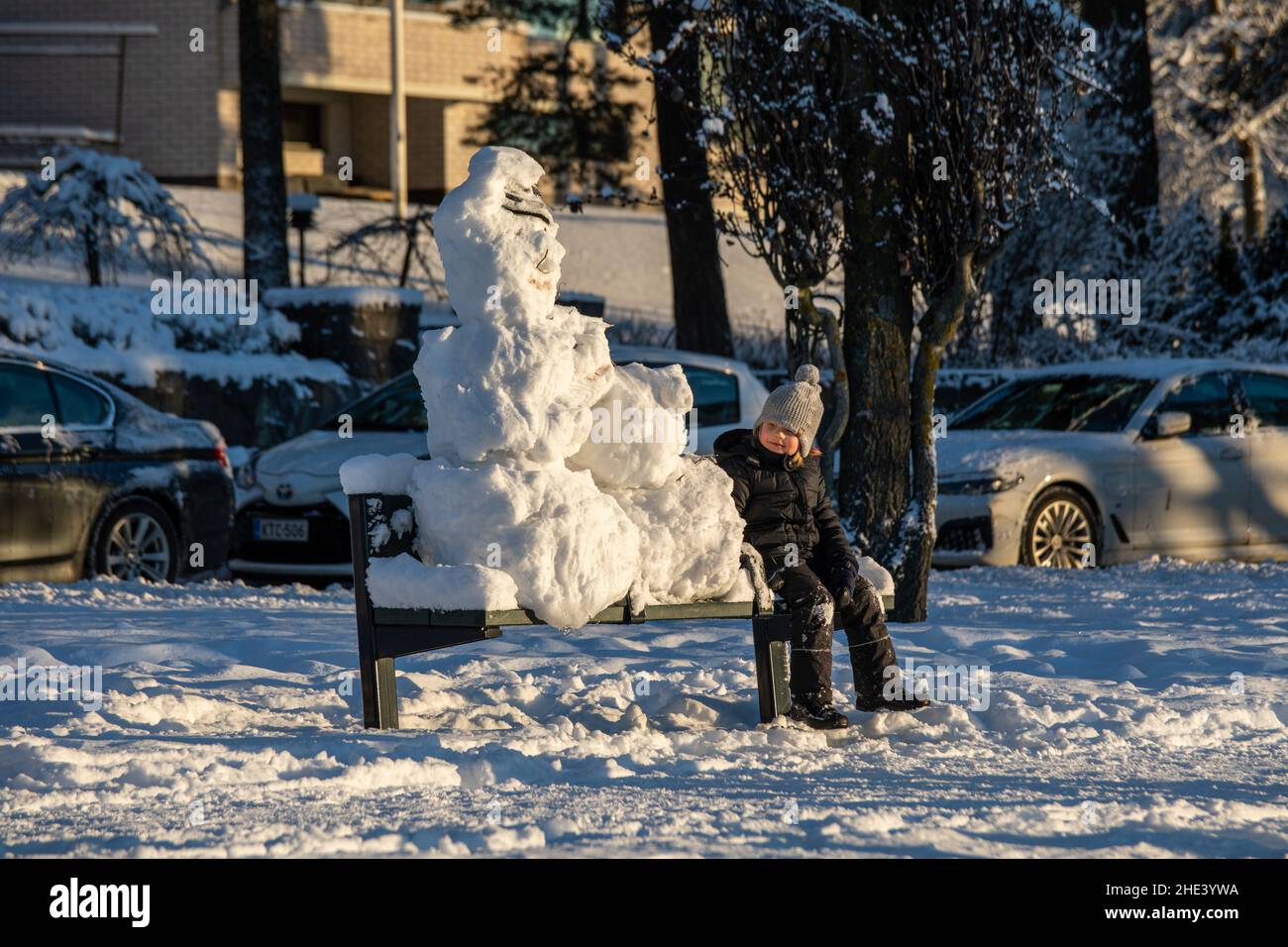 Enfant assis sur un banc de parc avec des bonhommes de neige lors d'une journée d'hiver ensoleillée dans le quartier de Munkkiniemi à Helsinki, en Finlande Banque D'Images
