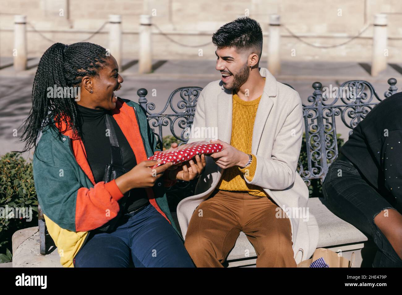 Homme heureux et femme échangeant des cadeaux tout en étant assis sur un banc à l'extérieur Banque D'Images