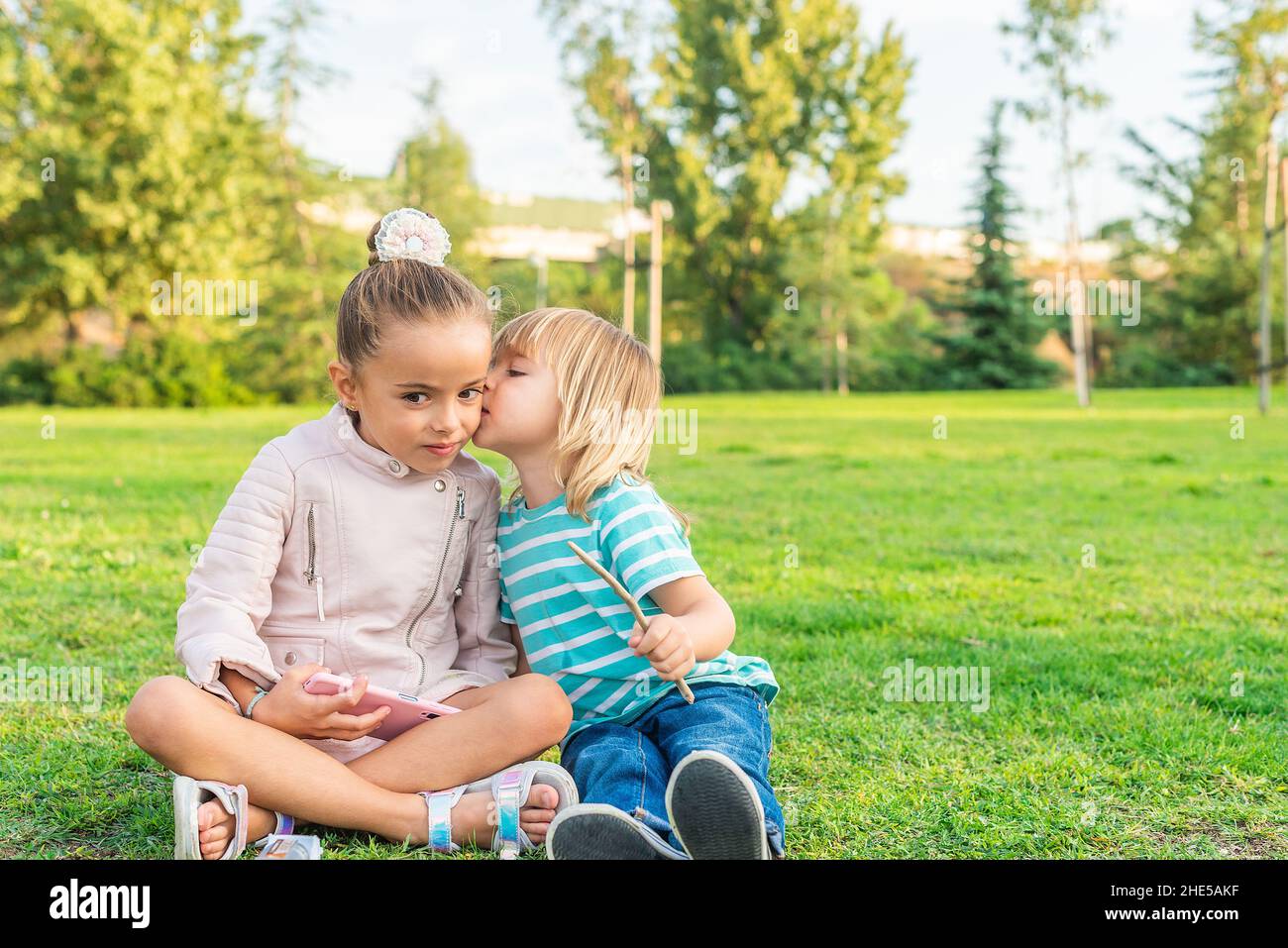 garçon assis sur l'herbe donnant à sa petite sœur un baiser Banque D'Images