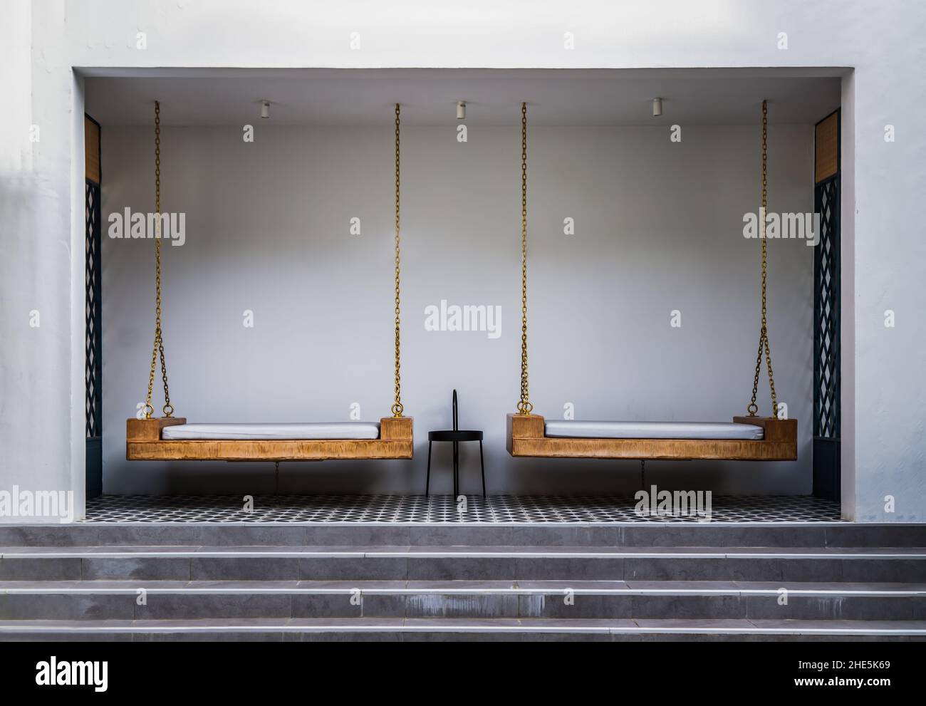 Chiang Rai,Thaïlande - 06 sept, 2020 : coin détente avec chaises balançoires en bois avec coussins de suspension sur la chaîne d'or et table latérale avec mur blanc Banque D'Images