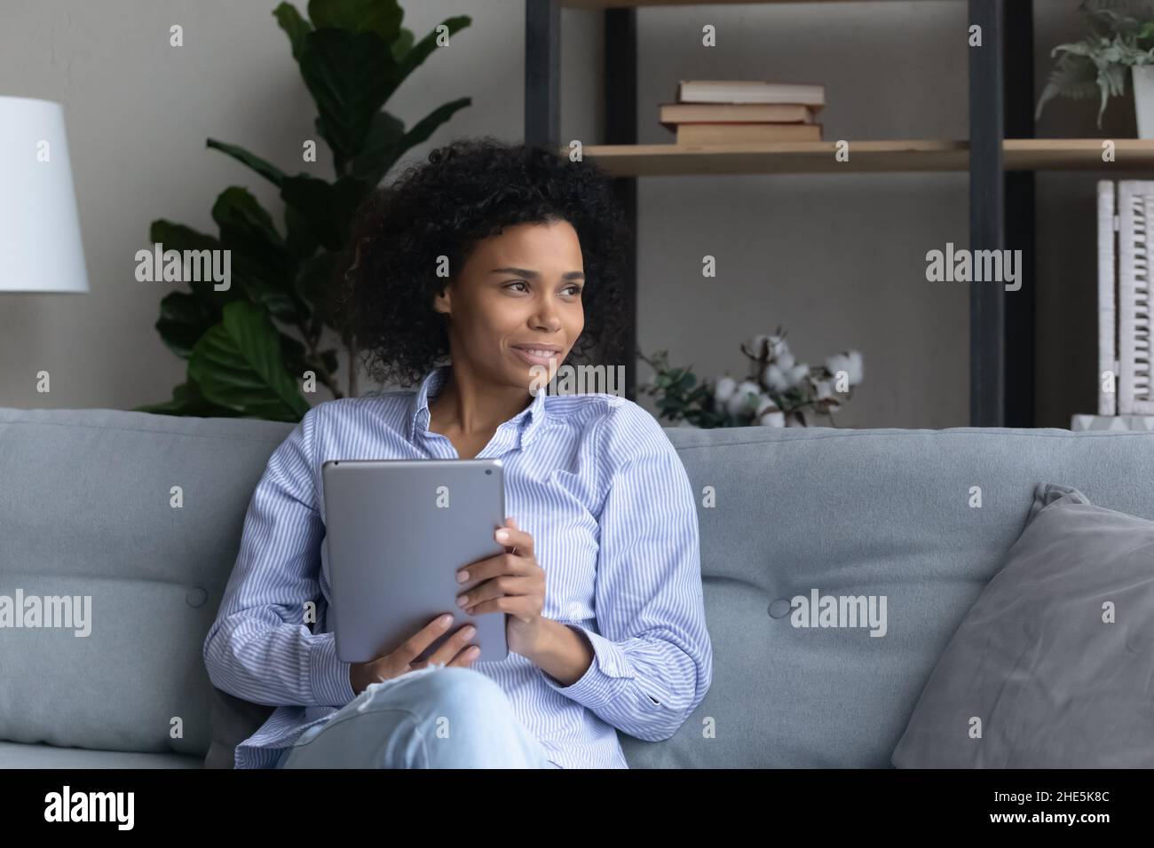 Jeune femme africaine rêveuse tenant une tablette numérique. Banque D'Images