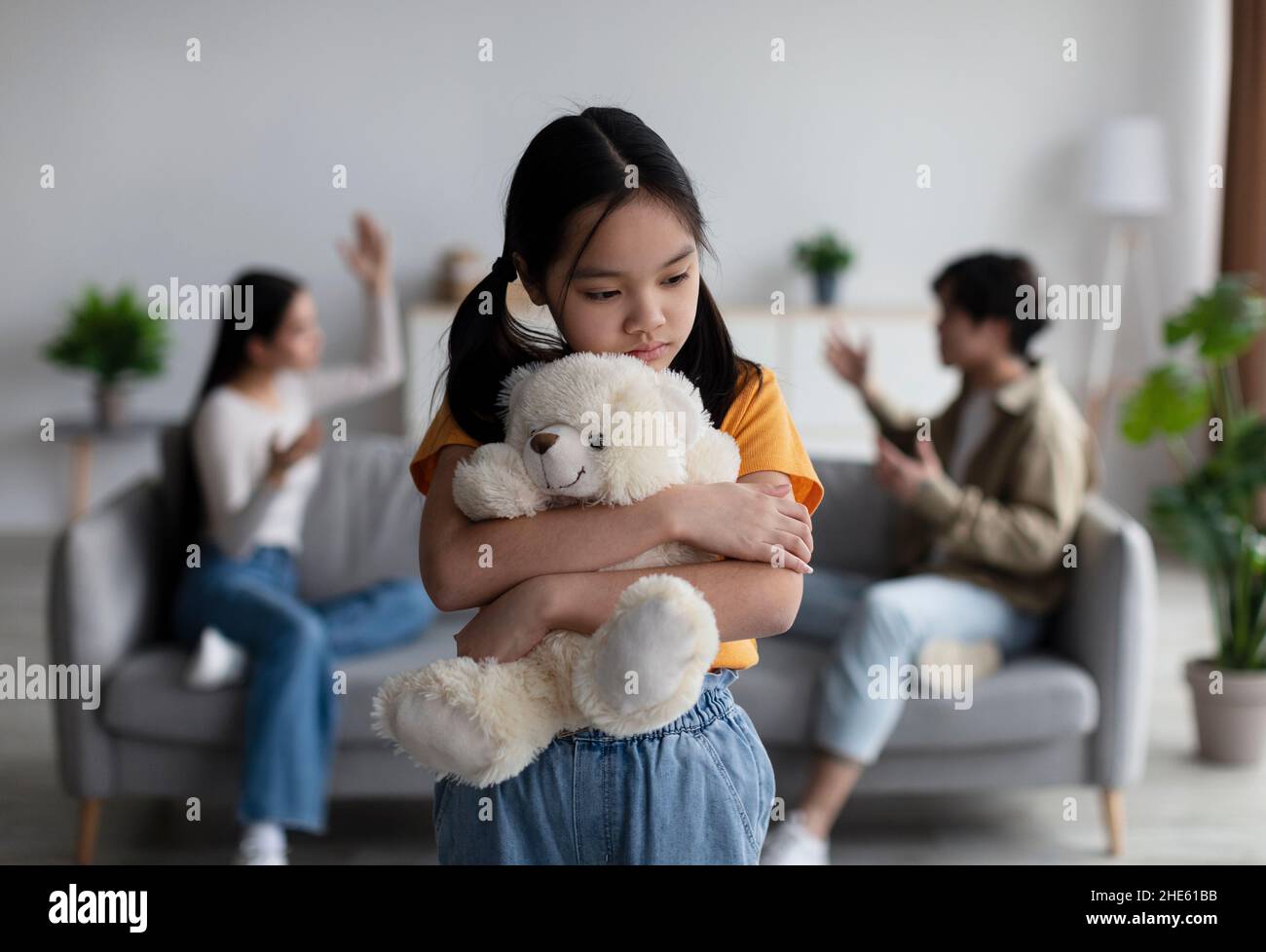 Triste malheureux malheureux desappairé coréen adolescente fille câlins jouet, parents querrel et de crier dans la salle de séjour intérieur, flou Banque D'Images