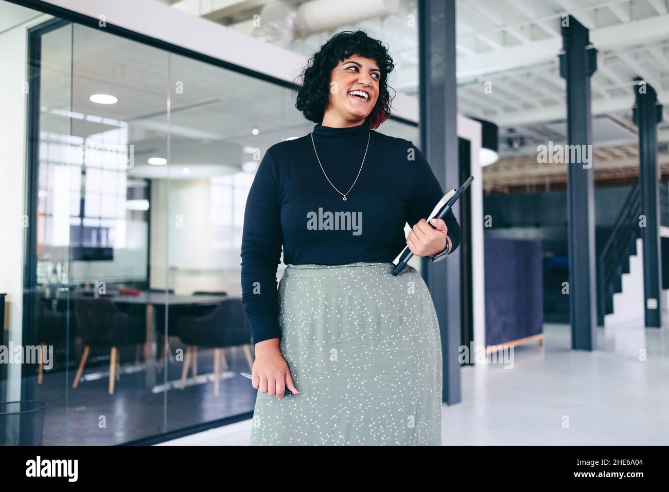 Femme d'affaires de taille moyenne qui regarde loin avec le sourire dans un bureau créatif.Bonne femme d'affaires tenant un pavé tactile numérique et un ordinateur portable tout en étant debout Banque D'Images Femme d'affaires de taille moyenne qui regarde loin avec le sourire dans un bureau créatif.Bonne femme d'affaires tenant un pavé tactile numérique et un ordinateur portable tout en étant debout Banque D'Images