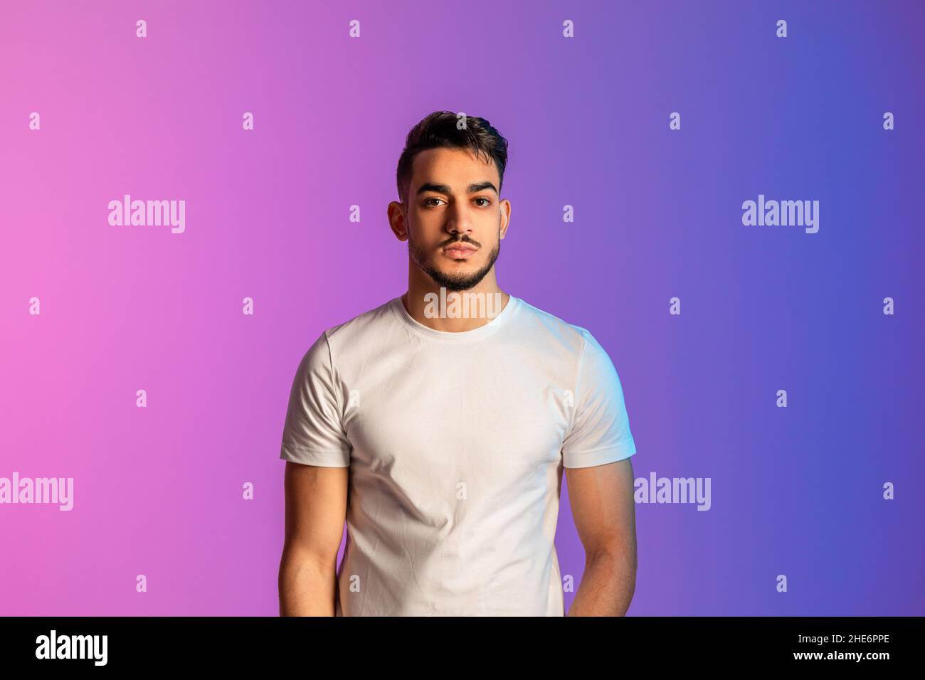 Portrait d'un beau jeune homme du Moyen-Orient ayant une expression sérieuse du visage, portant des vêtements décontractés à la lumière du néon Banque D'Images